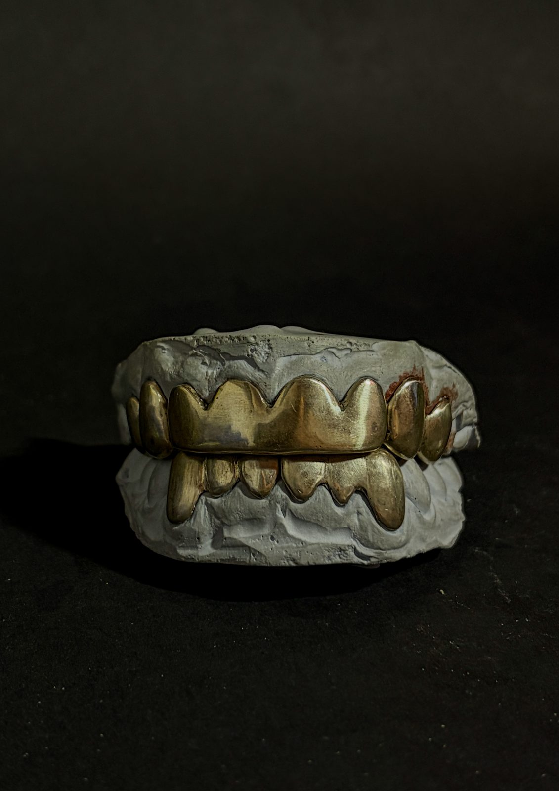 Handmade gold grillz resting on the plaster mold they were cast from